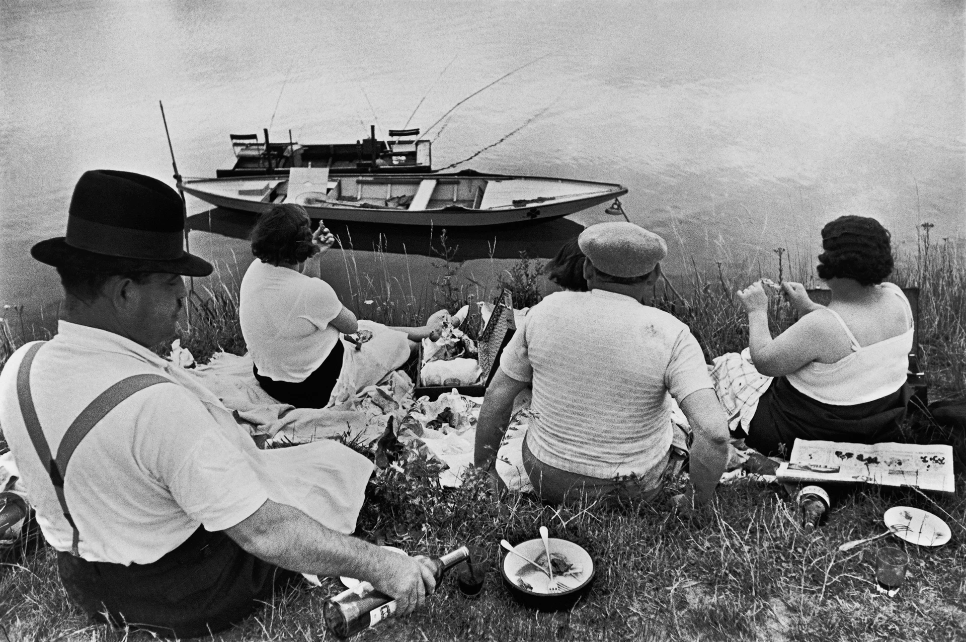 Imagen en blanco y negro, cuatro personas hacen un pícnic en un prado junto al río